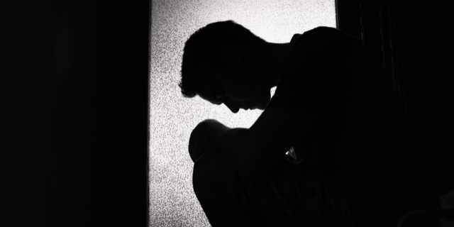 Silhueta de homem cabisbaixo e apoiado sobre os joelhos. 