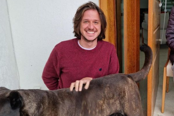 Cantor Rubel sorrindo com a mão em um cachorro marrom.
