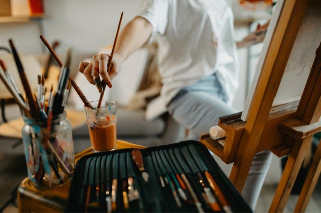 Mulher pintando molhando o pincel em um copo com água, para pintar a tela