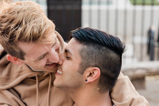 Imagem de um casal de homens sorrindo com o rosto colado