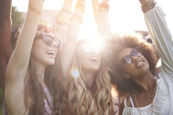 Amigas de óculos escuro com as mãos levantadas em um show