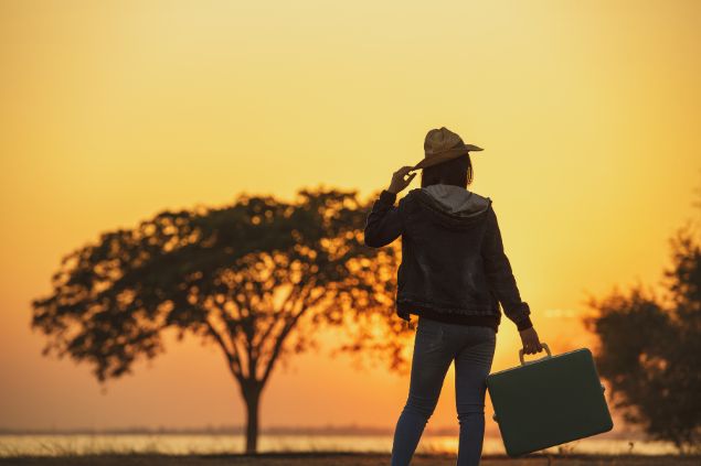 mulher com uma maça de viagem na mão ao pôr-do-sol