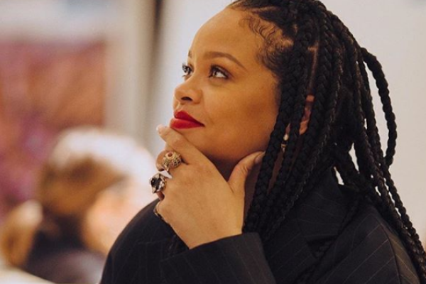 Rihanna sorrindo olhando para cima com a mão no  queixo 