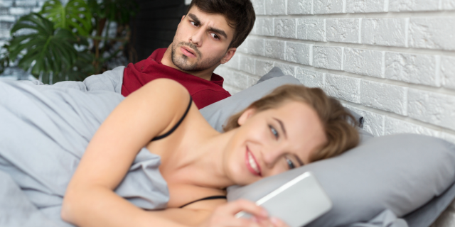 Homem olhando desconfiado para mulher mexendo no celular