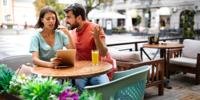 Homem discutindo com uma mulher. Ambos estão sentados em uma mesa de restaurante