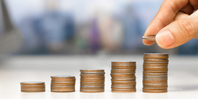 Mão colocando moeda em pilhas de moedas de tamanho crescente