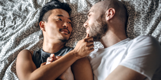 Dois homens deitados em uma cama, um olhando para o outro
