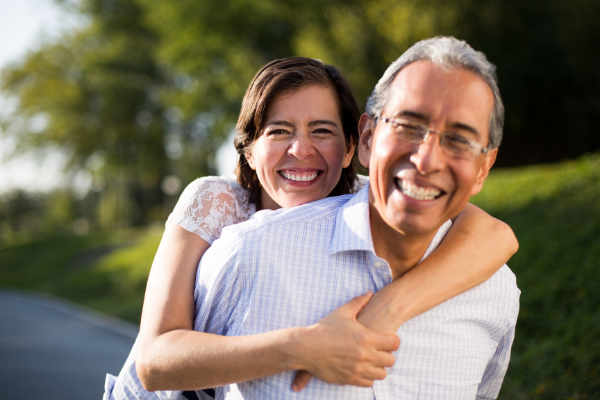 Imagem de um casal maduro. Os dois estão sorrindo e estão em um ambiente com árvores