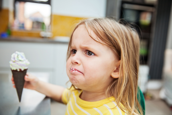 Criança com cara de birra segurando um sorvete de casquinha