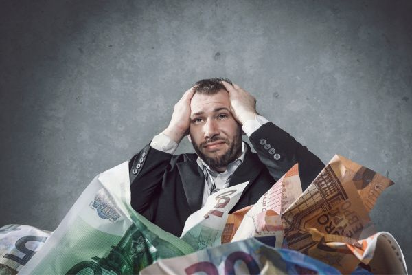 Homem com a mão na cabeça e dinheiro amassado, em sinal de dívida
