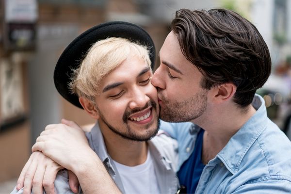 Casal abraçados e sorrindo, um dando beijo na bochecha do outro