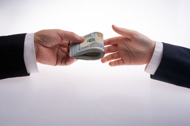 Imagem só da mão de um homem de terno entregando dinheiro para outro de terno
