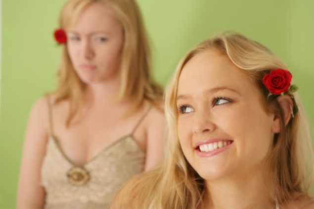 Imagem de uma moça sorrindo com uma flor atrás da orelha e outra olhando para ela com olhar de inveja