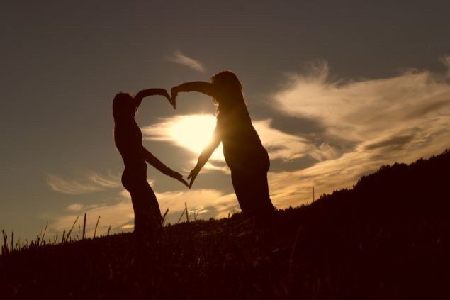 Imagem de duas pessoas ao ar livre fazendo um coração com os braços