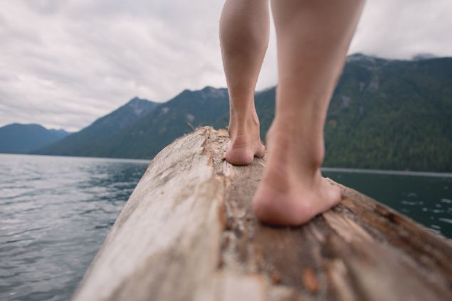 Imagem de uma pessoa atravessando um rio em cima de um tronco que está sobre as águas