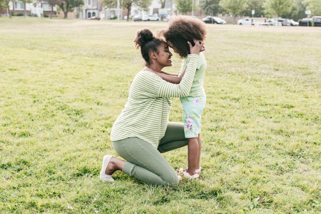 Imagem de uma mãe abraçando sua filha pequena, elas estão com as cabeças encostadas e sorrindo