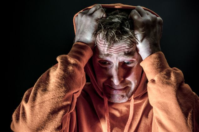 Imagem de um homem com expressão de angústia com as mãos na cabeça e de capuz