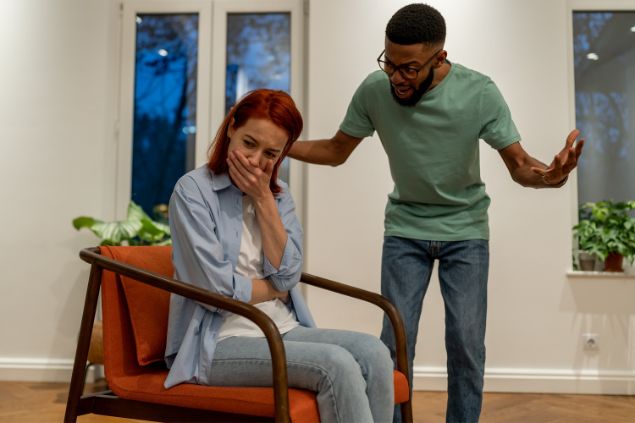 dimaberlinphotos/ Canva Pro Homem gritando com mulher que está sentada em uma cadeira e chorando com a mão na boca