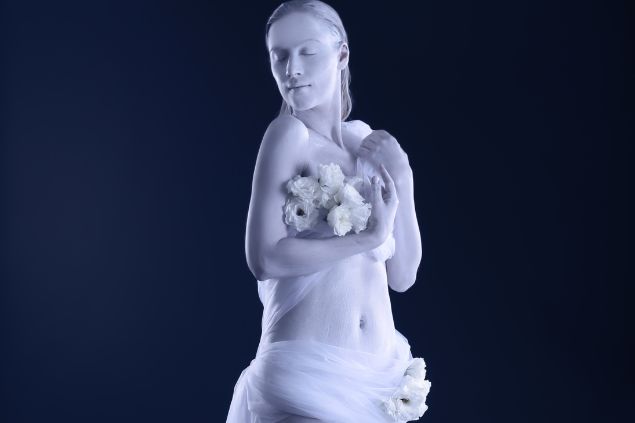 Mulher pintada de branco com os olhos fechados em um fundo preto