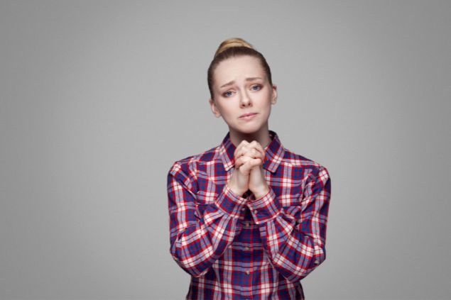 Mulher de frente para a tela com as mãos juntas e expressão de choro como se estivesse emplorando algo a alguém