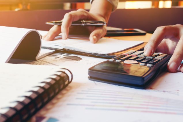 wutwhanfoto de Getty Images Pro/ Canva Pro Pessoa com uma caneta e bloco de anotações, fazendo cálculos em uma calculadora