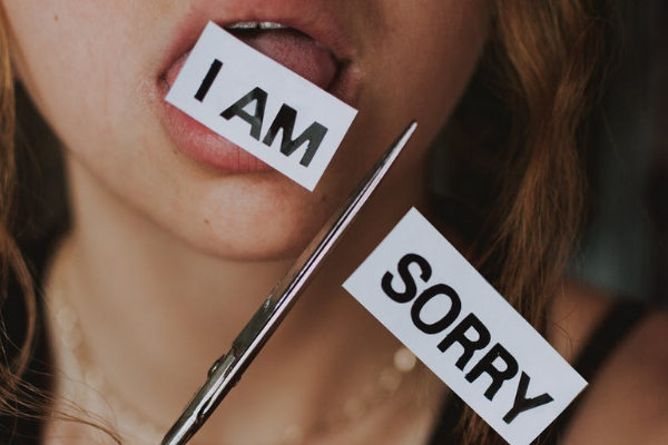 Mulher branca com papel na boca e tesoura na mão.