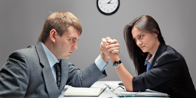 Homem e mulher em queda de braço em ambiente de trabalho. 
