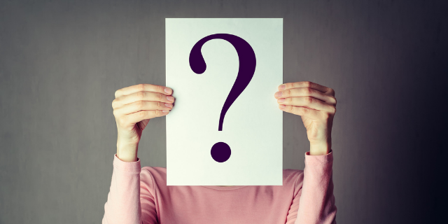 Mulher segura sobre seu rosto um papel com um ponto de interrogação.