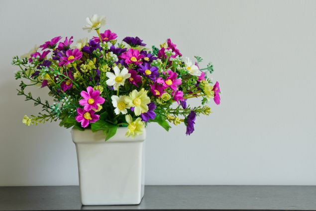 Flores coloridas e artificiais em vaso de enfeite, sobre fundo cinza. 