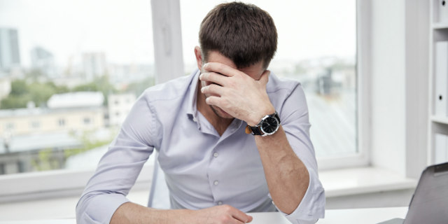 Homem preocupado com a mão direita apoiando a cabeça em cima de uma mesa de escritório