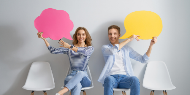 Um homem e uma mulher sentados lado a lado. Ambos seguram papéis cortados em formato de balão.