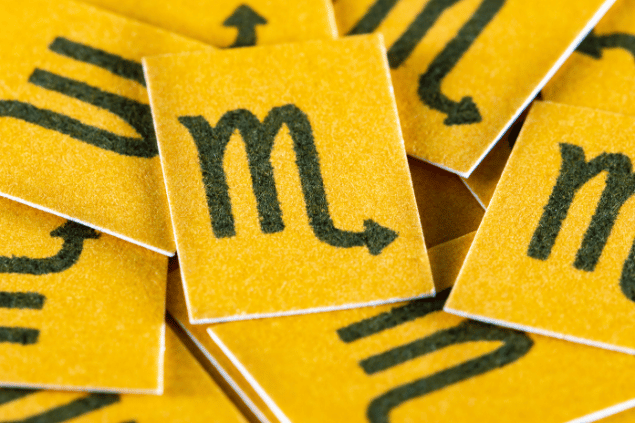 No foco da imagem, há vários pedaços de papel amarelo com o desenho do símbolo do signo de Virgem.