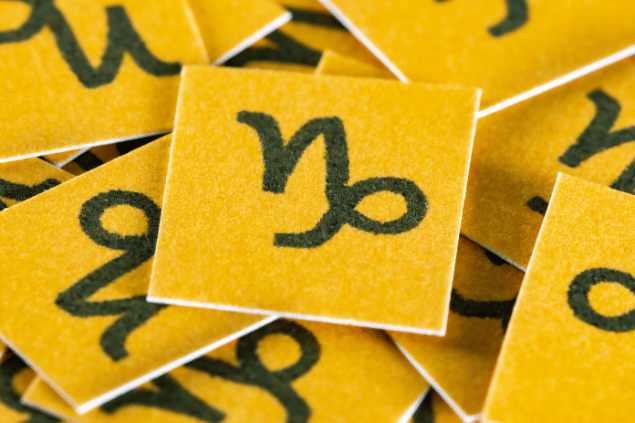 No foco da imagem, há vários pedaços de papel amarelo com o desenho do símbolo do signo de Capricórnio.