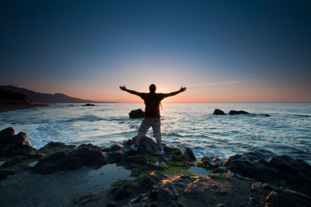 Homem na praia de braços abertos