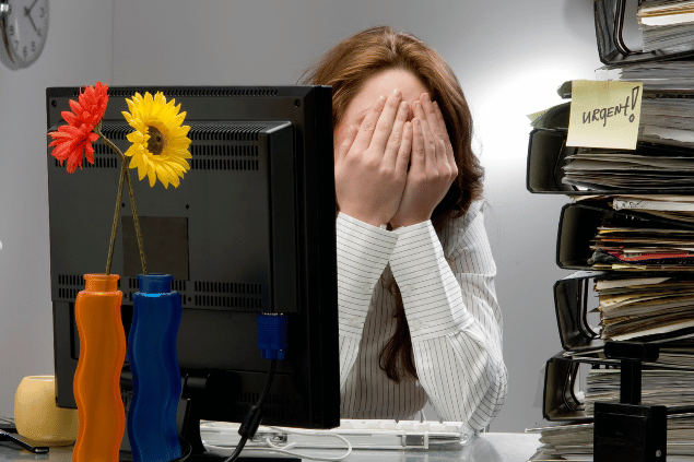 Mulher com a mão no rosto. Ao lado, vários trabalhos a serem feitos. 