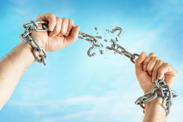 Mãos quebrando as correntes contra o fundo do céu azul.
