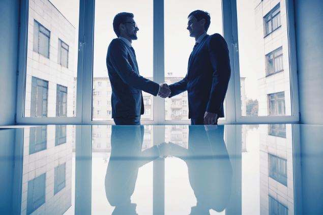 Homens vestindo terno em escritório, apertando as mãos em sinal de acordo. 