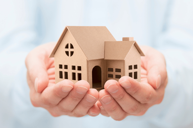Pessoa segurando miniatura de casa nas mãos. Conceito de aluguel ou compra de imóvel. 
