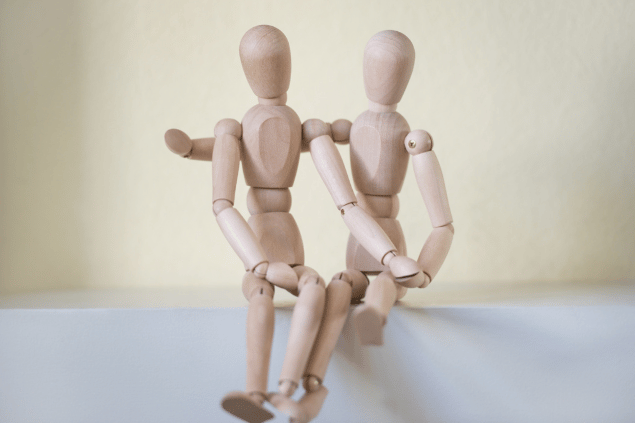 Bonequinhos de madeira sentados, enquanto se abraçam. Conceito de relacionamento. 