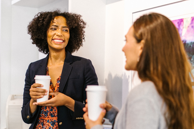 Duas mulheres sorrindo e conversando enquanto tomam um café