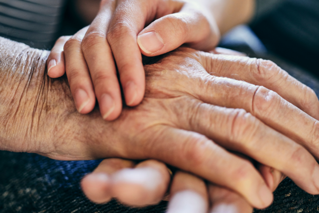 Uma mão jovem sob a mão de uma pessoa idosa