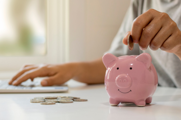 Pessoa colocando moeda em porquinho de porcelana