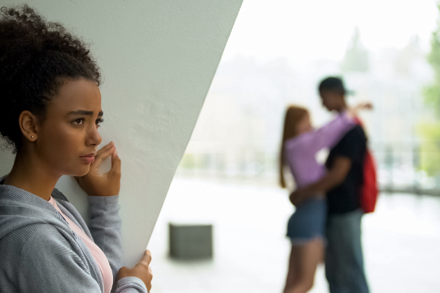 Mulher escondida atrás de uma viga observando um casal abraçado