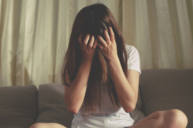 Mulher sentada no sofá com mãos na cabeça