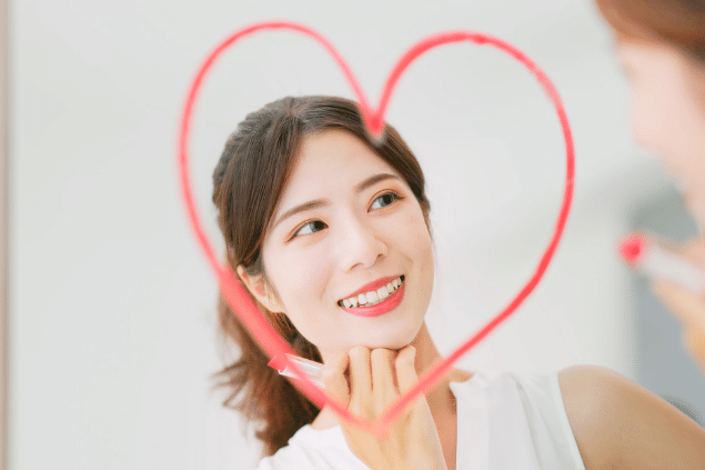 Mulher asiática desenhando um coração no espelho com seu batom