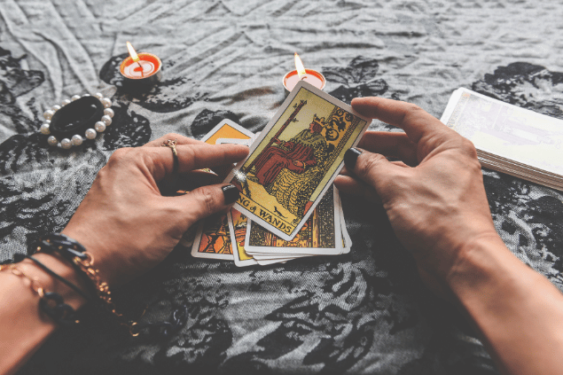 As duas mãos de uma taróloga ou vidente estão no centro da imagem. Ela segura uma carta do 