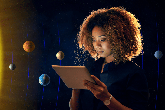 Imagem de uma mulher profissional que está trabalhando e lendo algo em um tablet. Ao fundo, há uma imagem do universo com os planetas do Sistema Solar.