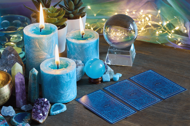Três cartas de Tarot, duas bolas de cristal, pedras e diversas velas estão sobre uma mesa.