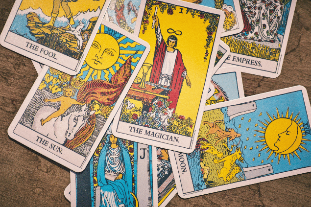 Algumas cartas de Tarot estão espalhadas sobre uma mesa. As cartas O Sol, O Mago e A Lua estão em destaque na imagem.
