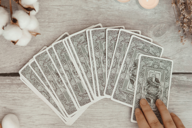 Um baralho de cartas virado para baixo está disposto sobre uma mesa. Ao lado dele, há velas e algodões.